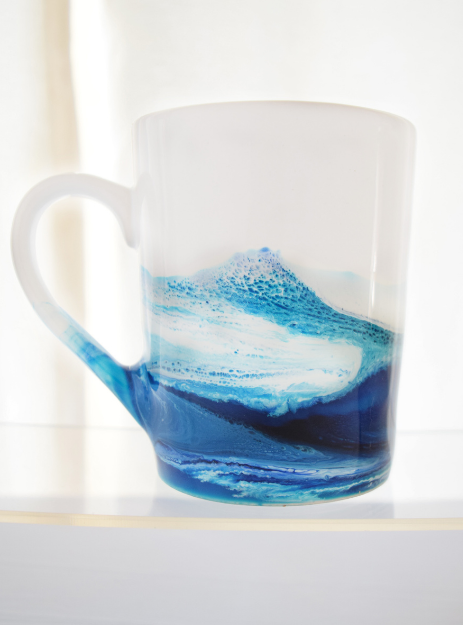 white mug hand painted with ocean blue waves sitting on table