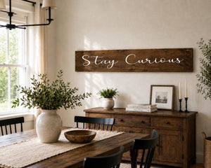 dark walnut 48 inch sign on wall with the words in white that say stay curious. in a dining room above a wood table.