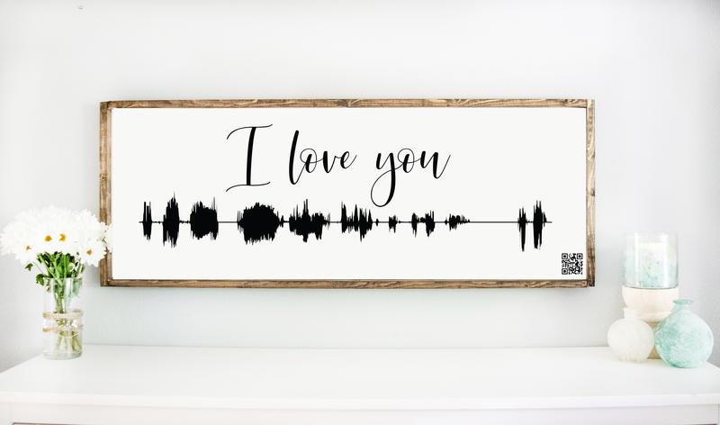personalized soundwave art with qr code that links to a video.  Words I love you in black lettering.  Large 48" X 18" white wood sign in frame above table with daisies.