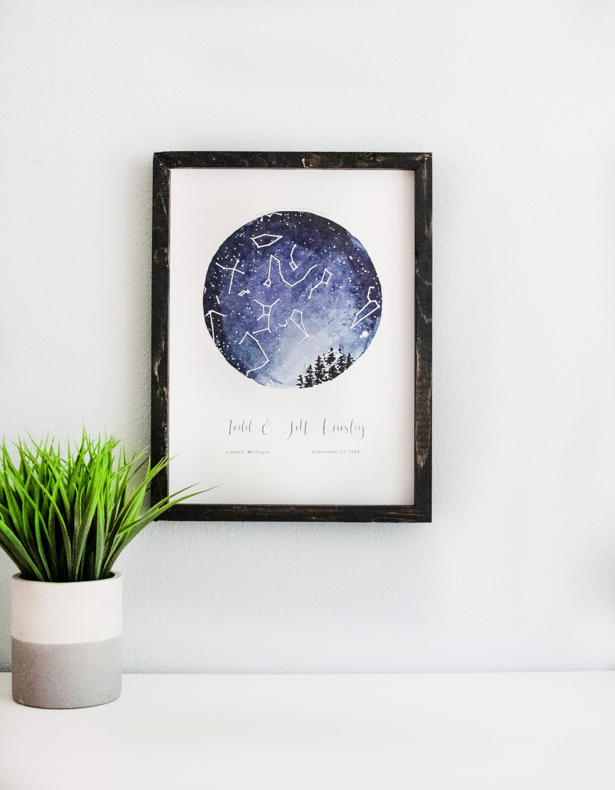 custom star map from a date and place in time.  blue circle with stars at that moment in time.  on white canvas in black frame on white table with plant.